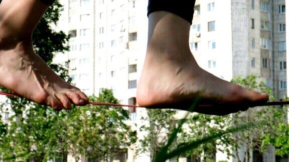 女人的腿在城市公园里沿着一条狭窄的线走着女脚在松弛绳一侧保持平衡