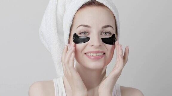 女士有着完美透明的皮肤头发用毛巾包着在眼罩下涂上黑色胶原蛋白