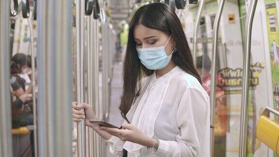 女商人在乘坐地铁时戴着保护面罩使用智能手机