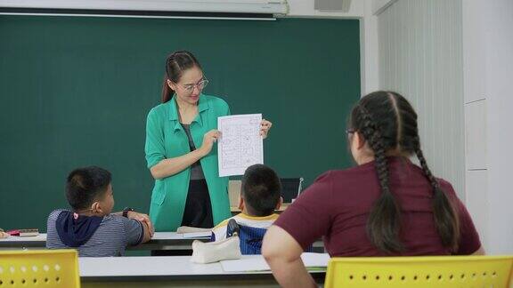 一个患有唐氏综合症的亚洲女孩集中精力学习回答英语问题在教室里与一个坐在轮椅上的残疾朋友一起完成作业后视镜里的姑娘们正幸福地坐在桌旁
