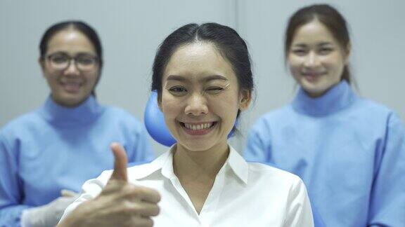 4K快乐的女病人竖起大拇指而牙医和助手在背景中微笑