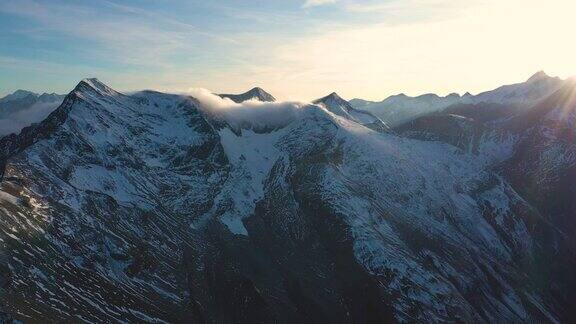 黄昏鸟瞰白雪覆盖的阿尔卑斯峰顶与夕阳的光束奥地利的霍赫陶恩国家公园