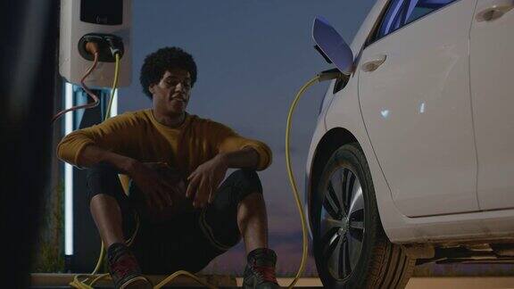 年轻的篮球运动员晚上在停车场给他的电动汽车充电