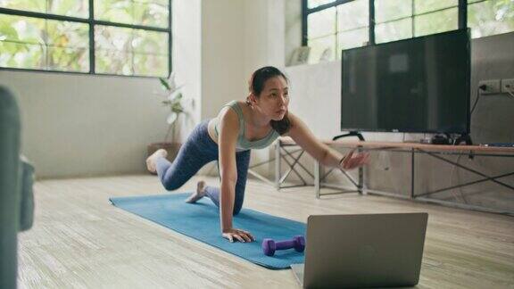 穿着运动服的年轻健身女士在家里的客厅里用笔记本电脑练习做初学者的锻炼