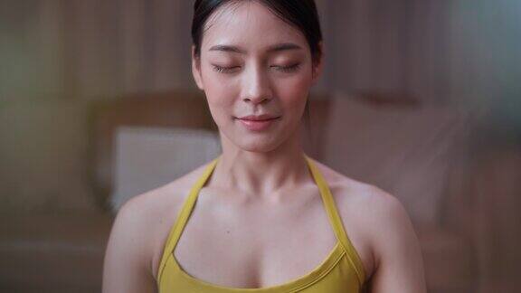 宁静的亚洲女性坐在地板上训练瑜伽在线在家练习瑜伽冥想和做呼吸练习吸气和呼气同时保持她的眼睛闭着