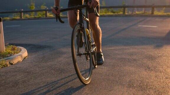 观看专业道路骑车人的双腿在日落时分骑着自行车上山