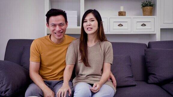 年轻的亚洲幸福夫妇看电视和喝咖啡在客厅的沙发上夫妇放松和花时间在一起在家里