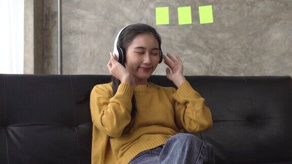 年轻的亚洲女性戴着耳机听着音乐在沙发上放松