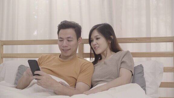 亚洲夫妇躺在床上玩手机在卧室里放松夫妇在家里用智能手机玩社交媒体夫妇使用在家放松时间