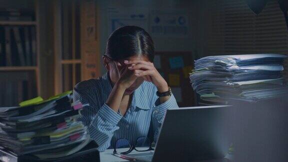 年轻的亚洲办公室员工感到疲倦疲劳精疲力竭而加班在办公室在晚上