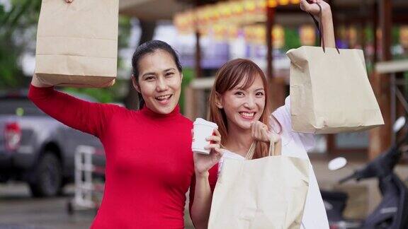 两名女士提着很多购物袋在人行道上微笑着看着镜头举起手臂