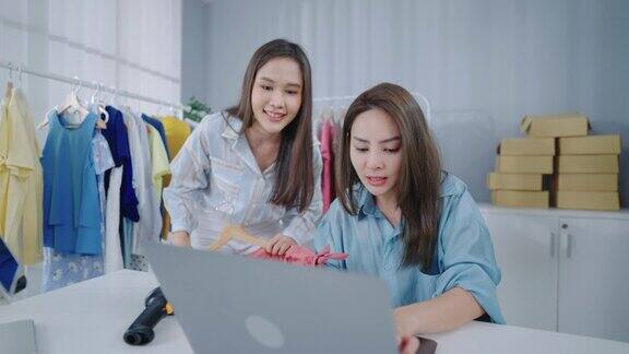两个自信的年轻女企业主坐在她的办公室里通过笔记本电脑上的直播向她的在线客户展示新的时尚商品