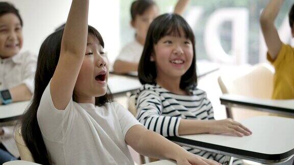 一群快乐的亚洲小学生在课堂上举起手臂回答老师的提问幼儿园学前概念