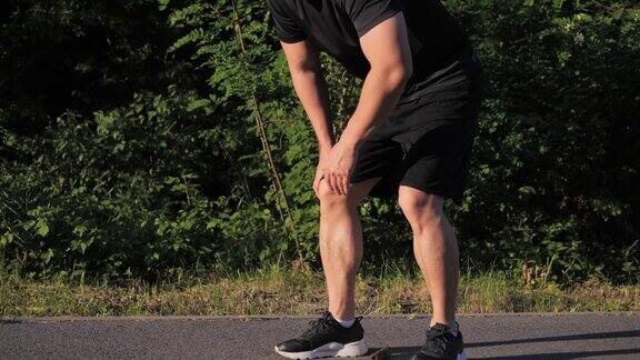 韩国男性慢跑者在慢跑时膝盖受伤疼痛正在按摩抽筋的腿部肌肉在公园里锻炼以绿树为背景夕阳西下身体状况膝盖疼痛