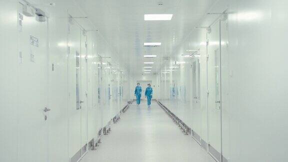 配戴防护口罩、身着防护服的女性走在制药厂大厅的总体规划医务人员在行走过程中交谈