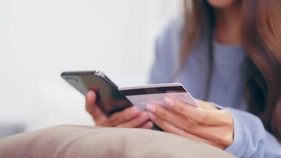 亚洲女性在家中客厅使用移动智能手机的手特写通过银行卡通过互联网进行网上银行支付用信用卡网上购物