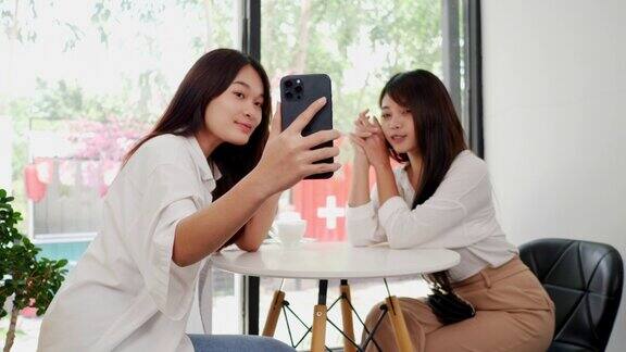 亚洲女子和朋友在咖啡店用智能手机自拍