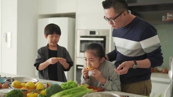 亚洲华人父女在厨房柜台边切橘子边和儿子一起吃饭