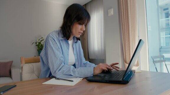 穿蓝衬衫的女人在家工作时使用笔记本电脑
