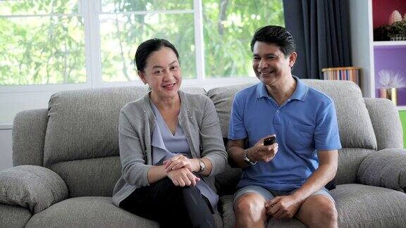 成熟的亚洲夫妇在家庭客厅的沙发上以激动的情绪为电视节目加油助威