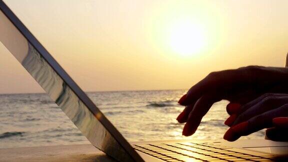 自由女性的手与笔记本电脑在日落或日出的背景自由职业者远程工作在海上工作和度假