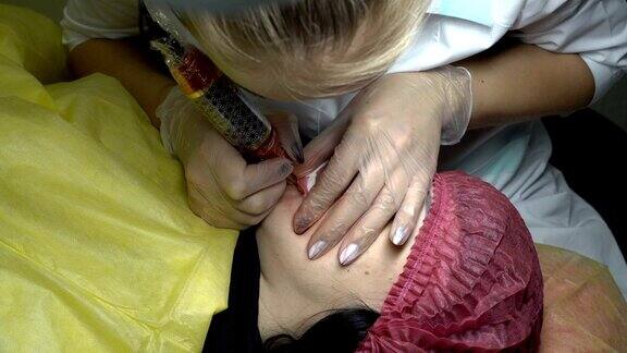 在美容院里一位女士正在给下唇做纹身专业美容师用针在女人的嘴唇上涂颜料