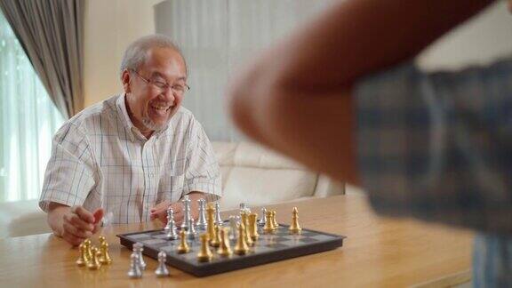 亚洲老年男性花休闲时间退休后呆在家里快乐的微笑老人喜欢在家里和朋友一起下棋医院保健和医疗理念