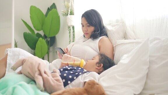 4K亚洲母亲一边用手机给躺在床上的小女儿喂奶一边给她喂奶