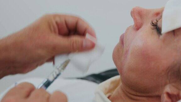 特写医生的手正在填补注射与透明质酸在鼻唇沟痛苦的美容手术的一个女人的脸在美容医疗诊所