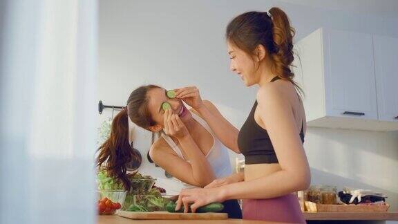 两个穿着运动服的亚洲年轻女子在厨房里做沙拉活泼漂亮的女孩姐姐感到快乐喜欢吃蔬菜健康的食物来减肥在家里的保健