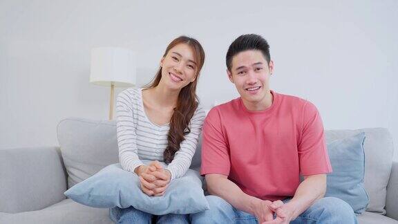 亚洲年轻夫妇坐在客厅沙发上的肖像有吸引力的浪漫的新婚姻男人和女人微笑着看着相机享受在情人节在家里一起度过的时间