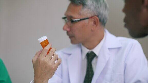 亚洲男性医生向护士和他的病人展示一瓶药片