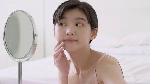 美丽的年轻亚洲女人微笑看着镜子检查脸与皮肤护理和美容年轻化和卫生美丽的女孩快乐清洁面部与霜或乳液和健康