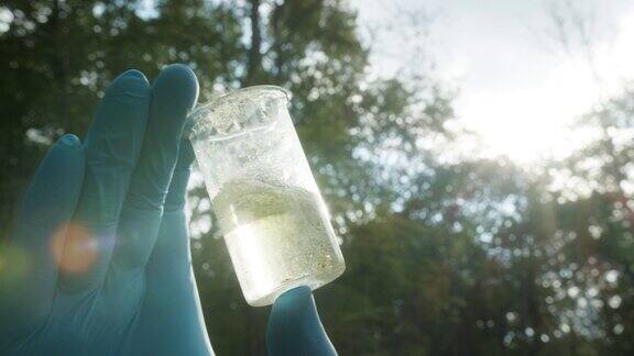 穿着个人防护装备的化学家看着装有溶液的烧瓶从沼泽中进行水分析穿着防护服和医用手套进行毒性测试的样品科学研究实地实验室理念