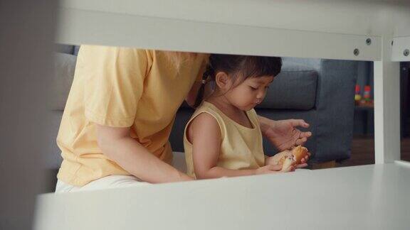 快乐快乐的亚洲家庭妈妈和蹒跚学步的女孩吃着甜甜圈在家里客厅的沙发上放松享受
