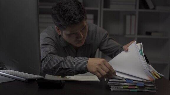 亚洲男性商人在办公室用财务文件和台式电脑工作到很晚加班的年轻人工薪族概念4k