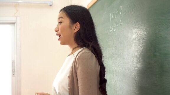年轻的亚洲女教师在黑板上写数学算术题