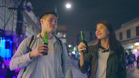 亚洲帅哥情侣一起喝酒开派对在城市里旅游的青年男女在假期里一起拿着一瓶啤酒在漆黑的夜晚在路上度过时光