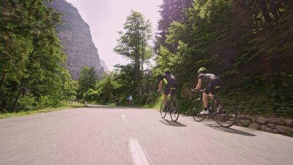 TS两名男性公路自行车骑在三个骑自行车的朋友后面沿着风景如画的山路