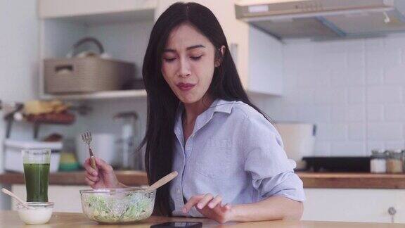 年轻健康的亚洲女性在家里厨房的桌子上吃沙拉蔬菜使用智能手机上的应用程序节食日体重计算卡路里