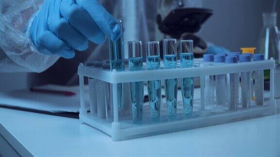 科学家或医护人员穿着防护服拿着带有蓝色试剂的试管装有化学液体的实验室玻璃器皿显微镜实验室生物化学医学和研究概念