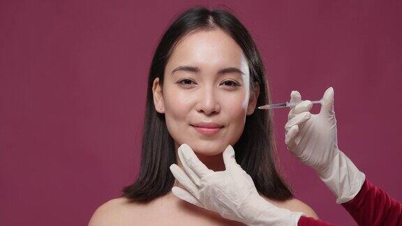 年轻的亚洲妇女高兴的医生戴着手套试图给她的脸注射对玛萨拉copyspace