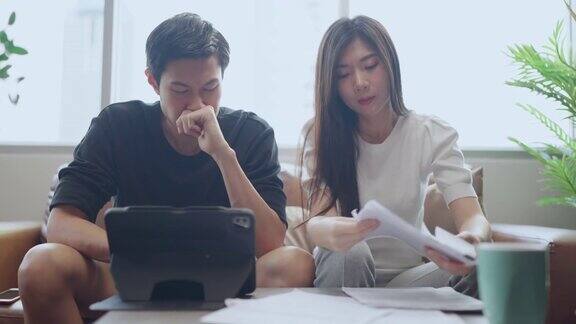 亚洲结婚夫妇在沙发上一起检查和计算财务账单涉及财务文书工作在客厅的家庭背景使用电子银行笔记本电脑在线纳税