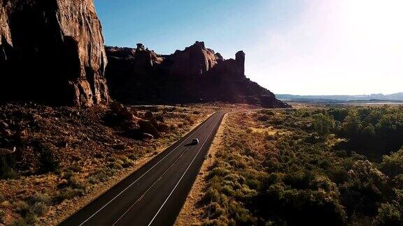 无人机摄像头在日落美国沿着沙漠公路行驶的汽车靠近惊险的陡峭峡谷山脊
