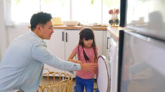 亚喜一家人呆在家里爸爸教女儿洗脏衣服小可爱的小女孩帮助和学习父母爸爸把衣服放在洗衣机电器在家里Domestic-Housekeeping