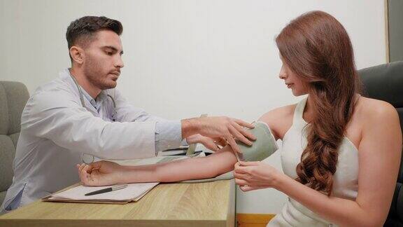 穿着白大褂的亚洲男性医生在美容诊所或医院的保健部门用血压计测量美丽的年轻亚洲病人的手臂血压并记录在医疗申请表上