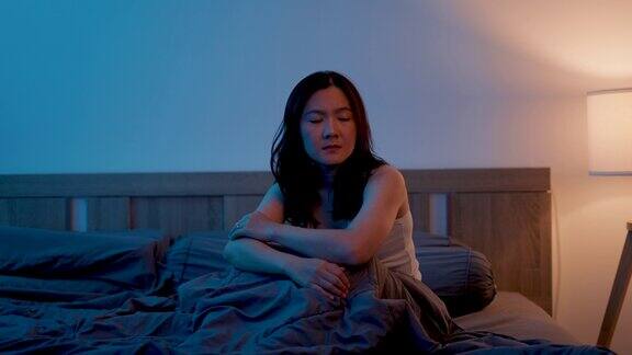 亚洲女人感到悲伤坐在床上抱着膝盖思考问题