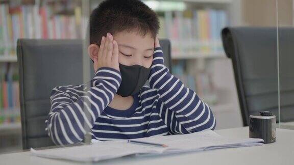 一个亚洲小男孩坐在图书馆里做作业发呆无聊不想工作