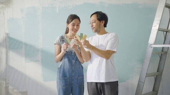 年轻的亚洲夫妇选择他们的新墙壁房间的颜色粉刷墙壁