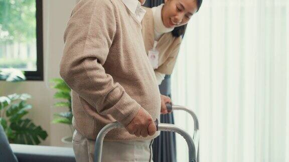 年轻的亚洲女性护理人员教老男性走路使用助行器照顾在家里的客厅握着老人的手